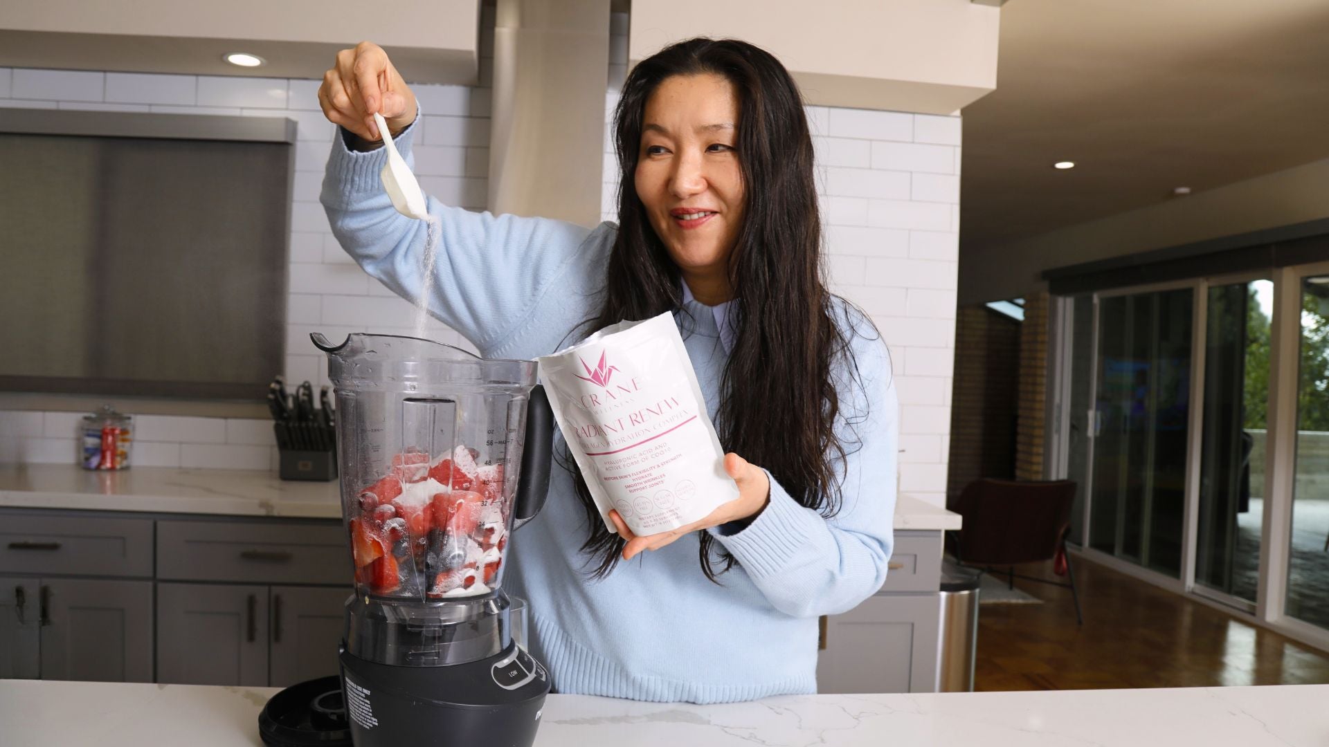woman in kitchen mixing collagen powder into blender and making a smoothie